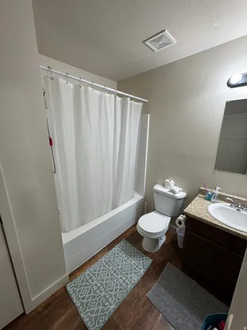 Full bath featuring a textured wall, vanity, dark wood-style floors, a textured ceiling, and shower / bath combo
