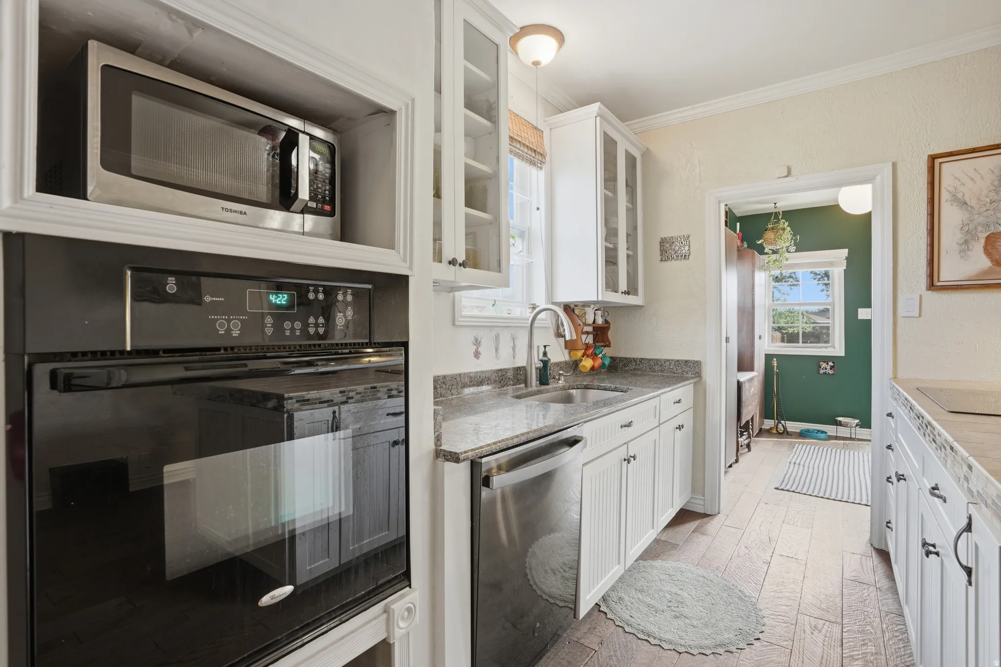 Kitchen with stainless steel appliances, glass insert cabinets, light stone countertops, white cabinetry, and ornamental molding