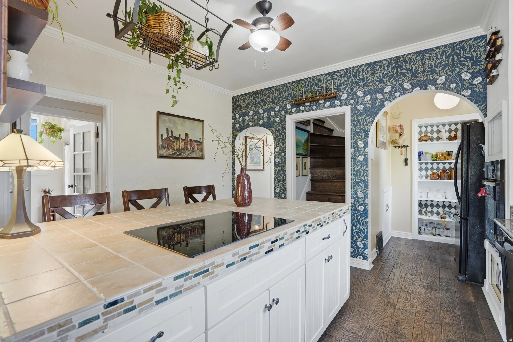 Kitchen with tile counters, dark wood-style flooring, crown molding, a kitchen bar, and black appliances