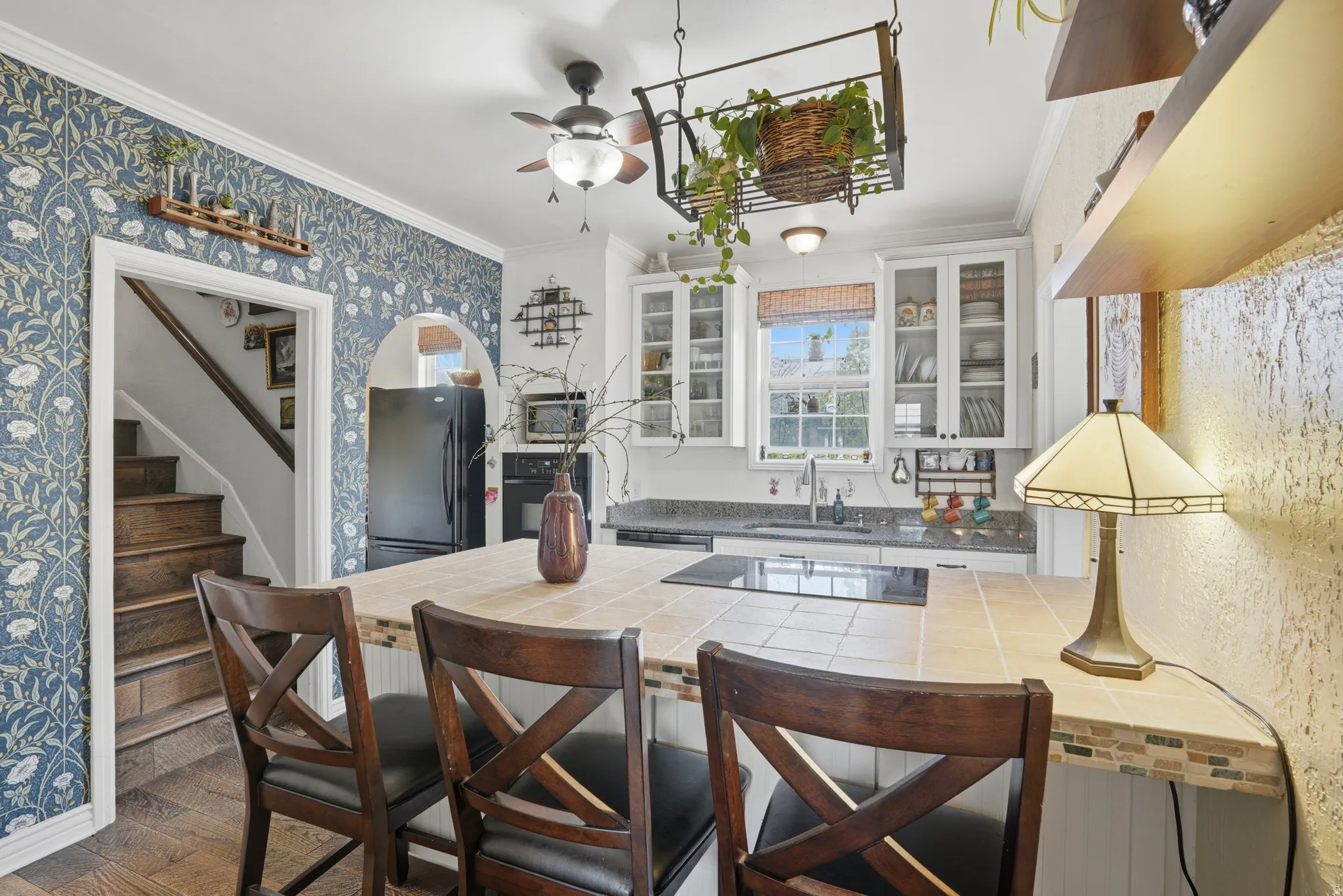 Kitchen with tile countertops, ornamental molding, black appliances, glass insert cabinets, and white cabinetry