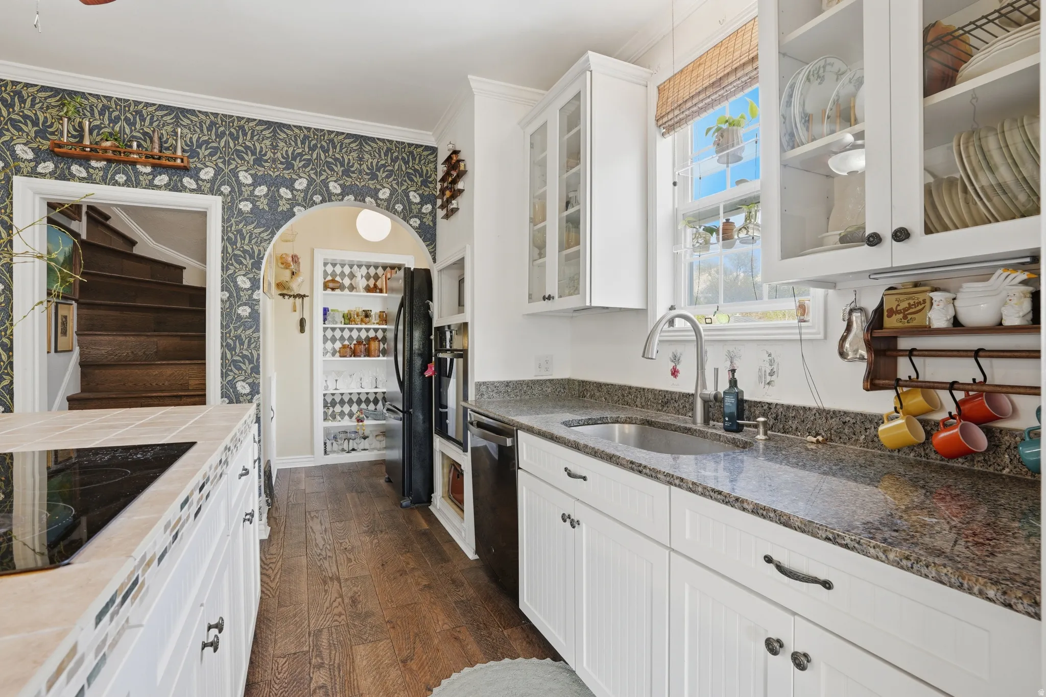 Kitchen featuring wallpapered walls, glass fronted cabinets, dark wood finished floors, white cabinetry, and arched walkways