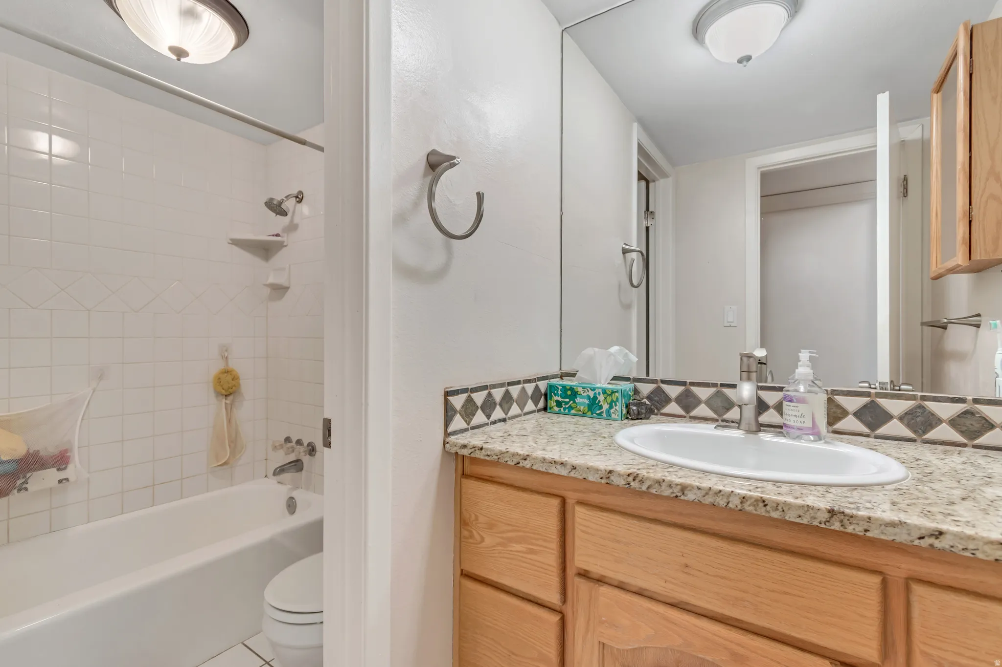 Bathroom with bathing tub / shower combination, vanity, decorative backsplash, and tile patterned floors