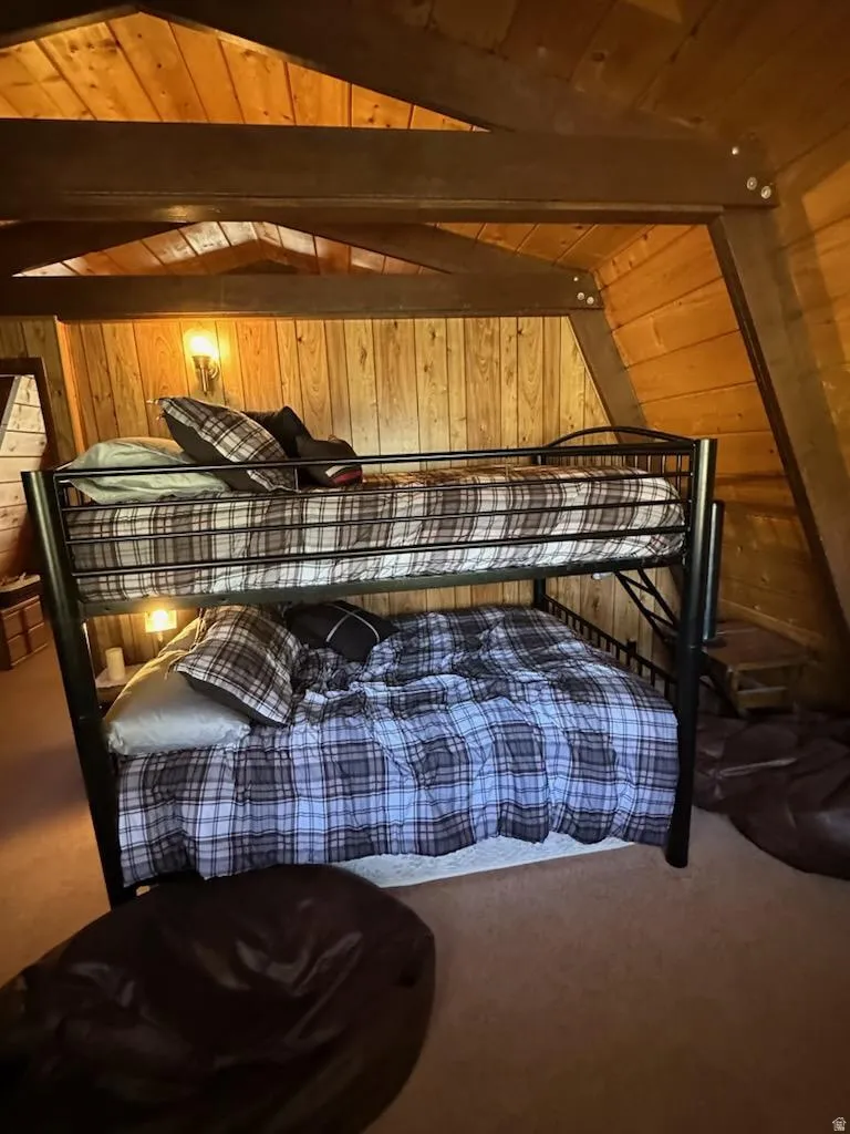 Bedroom featuring carpet floors, wooden walls, lofted ceiling with beams, and wooden ceiling