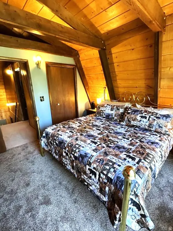 Bedroom with lofted ceiling with beams, wood ceiling, carpet floors, and wooden walls