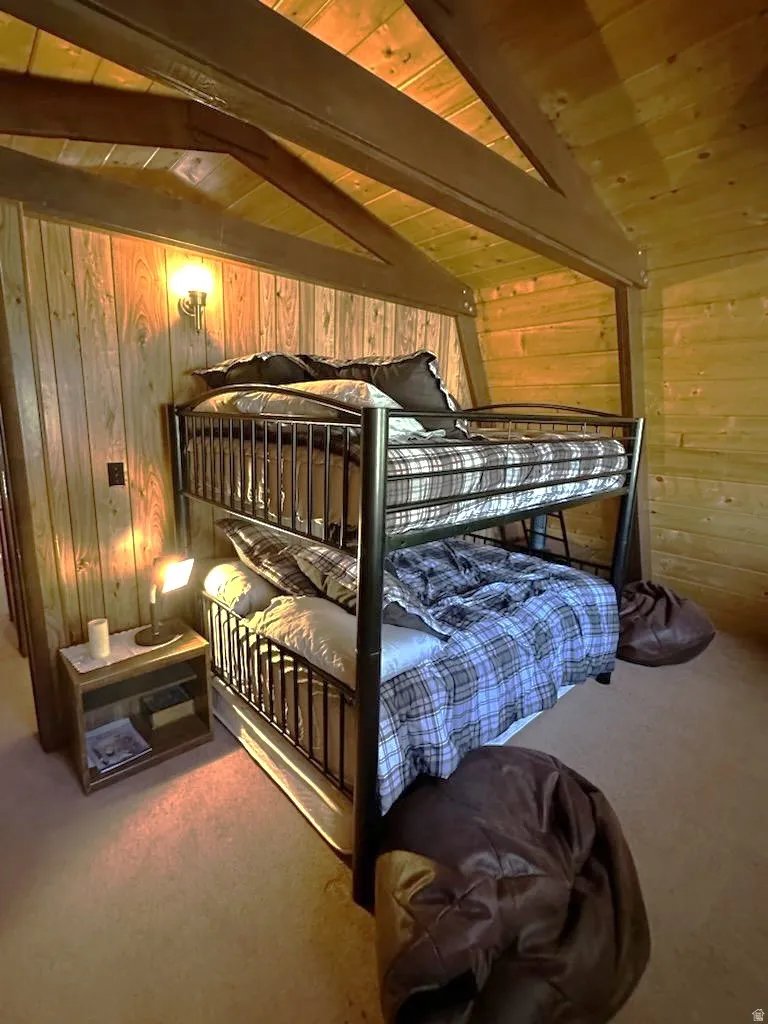 Bedroom featuring light carpet, wooden walls, vaulted ceiling with beams, and wooden ceiling