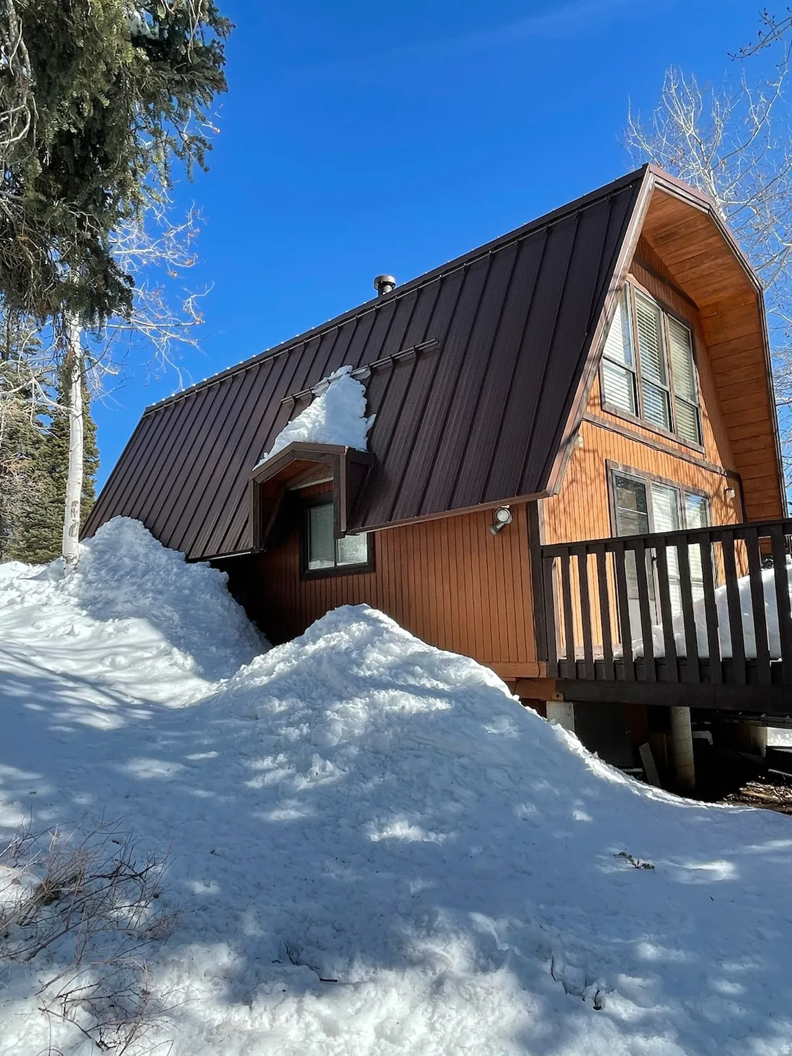 Snow covered property with a wooden deck, a gambrel roof, and a metal roof