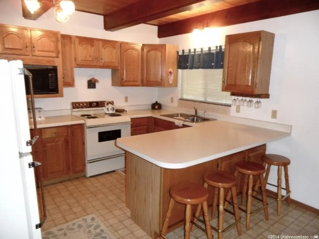 Kitchen with a breakfast bar area, a peninsula, white appliances, light countertops, and light flooring