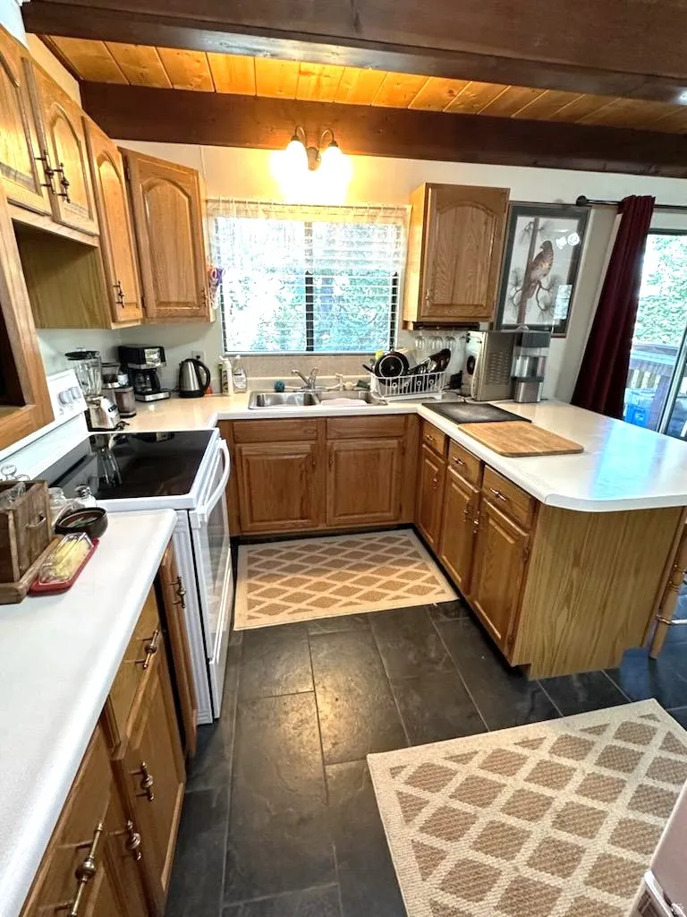 Kitchen featuring white electric range, a peninsula, light countertops, wood finish cabinets, and a wooden ceiling with exposed beams