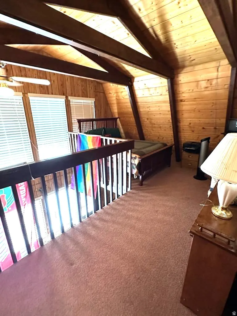 Carpeted bedroom featuring wood walls, lofted ceiling with beams, and wooden ceiling