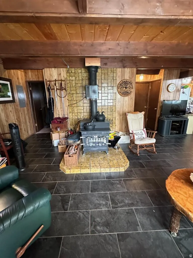 Living area featuring wooden walls, a wooden ceiling with exposed beams, and a wood stove