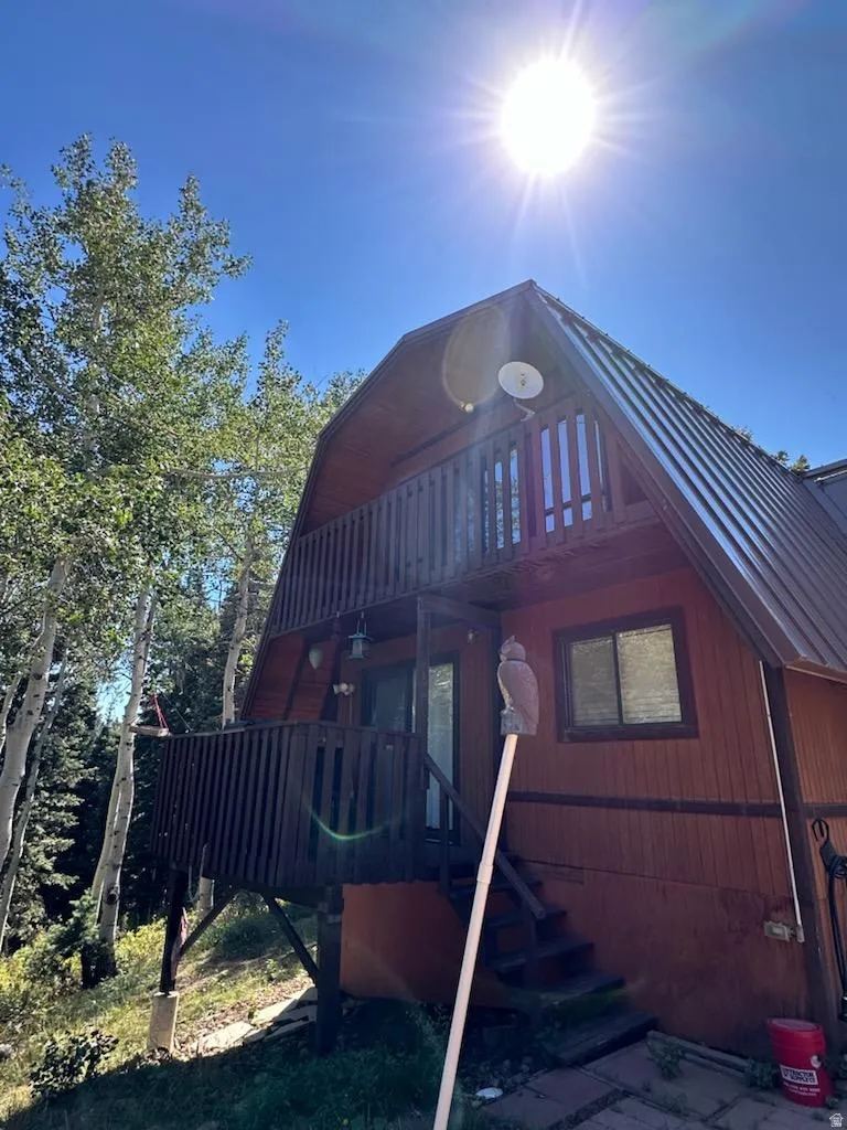 View of side of home featuring a gambrel roof, a balcony, and a wooden deck