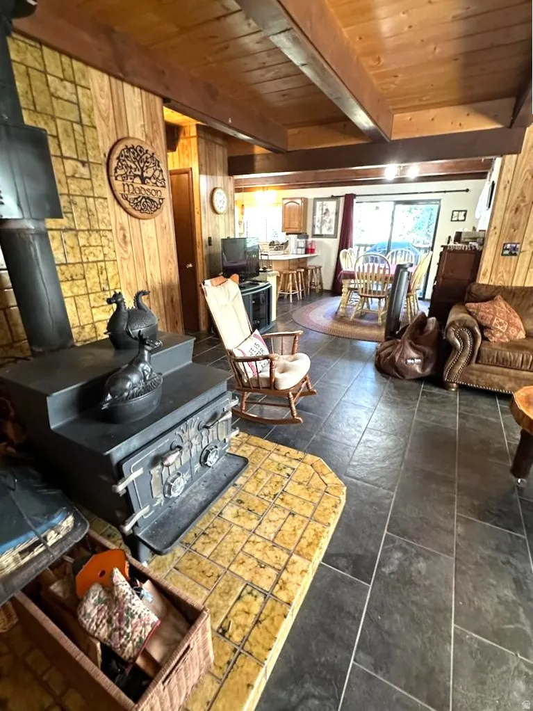 Living area with a wood stove, wood walls, and a wood ceiling with exposed beams