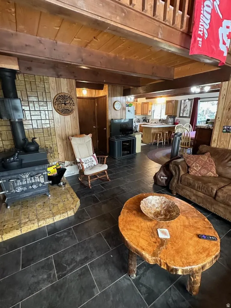 Living area with wood walls, a wood stove, and a wood ceiling with exposed beams