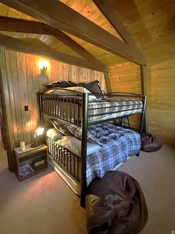 Bedroom featuring light carpet, wooden walls, vaulted ceiling with beams, and wooden ceiling