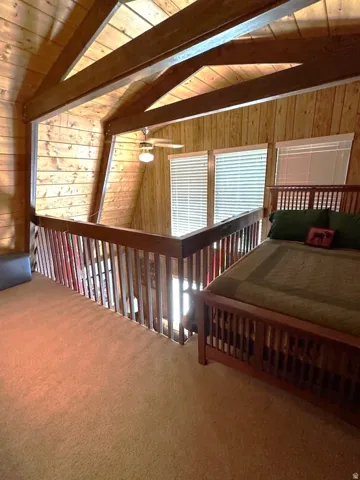Carpeted bedroom featuring wooden walls, wooden ceiling, and lofted ceiling with beams