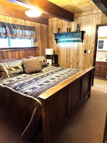 Carpeted bedroom with wood walls and a wood ceiling with exposed beams