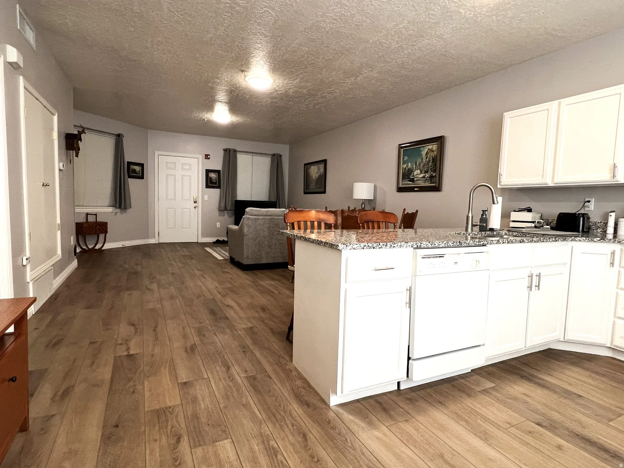 Kitchen with a peninsula, a textured ceiling, white dishwasher, open floor plan, and light stone countertops