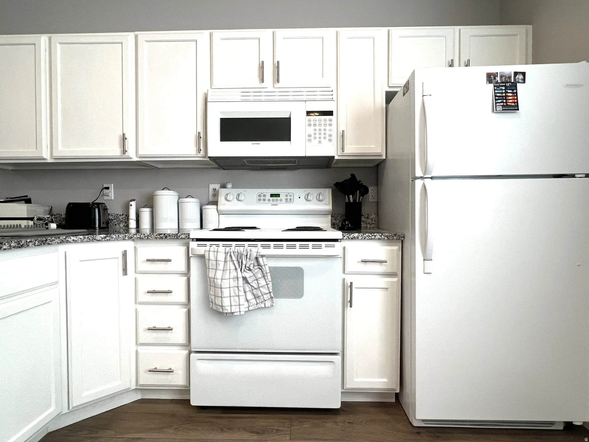 Kitchen with white cabinets, white appliances, dark wood-style flooring, and dark stone counters