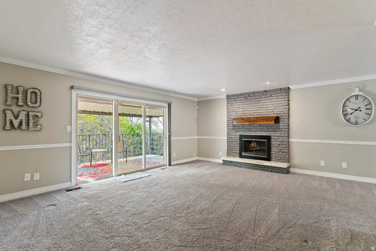 Spacious living area featuring a stone-clad fireplace with a wood mantel, a sliding glass door providing outdoor access, and neutral wall tones with white trim