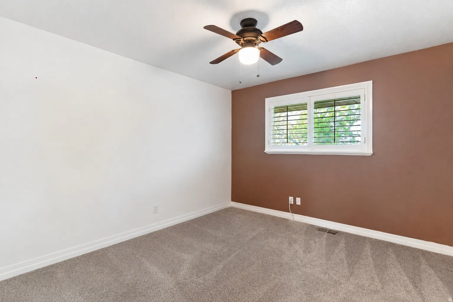 Bedroom featuring a ceiling fan, window with white plantation shutters, and carpet flooring