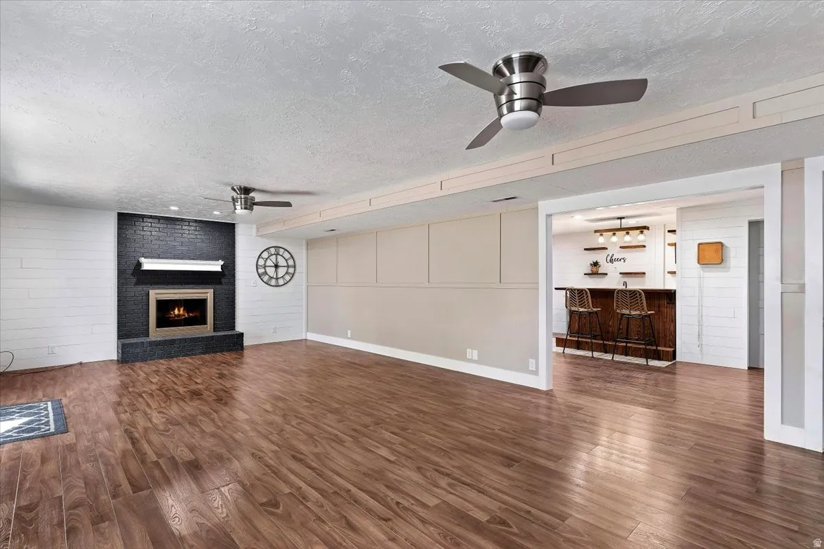 Unfurnished living room featuring a textured ceiling, dark wood-type flooring, a fireplace, ceiling fan, and wood walls