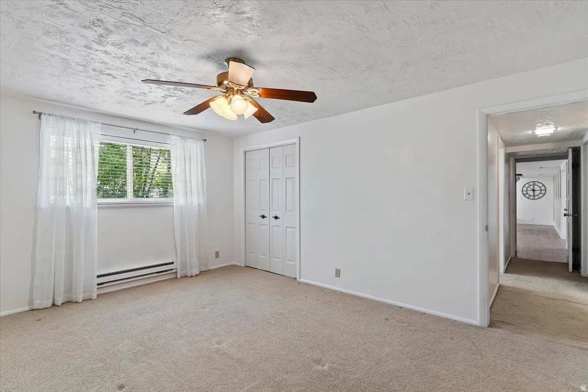 Unfurnished bedroom featuring carpet floors, a textured ceiling, a baseboard heating unit, a closet, and ceiling fan