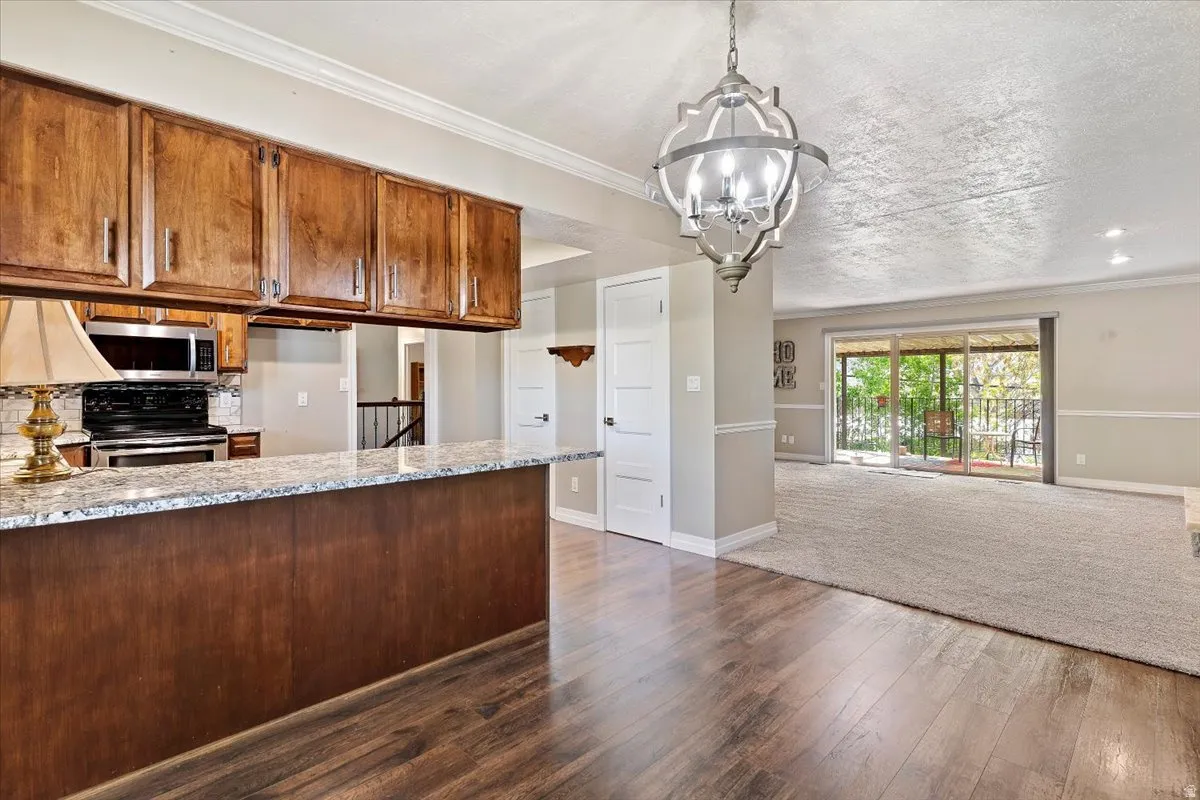 Kitchen featuring stainless steel electric range, dark wood finished floors, a textured ceiling, wood finish cabinets, and ornamental molding