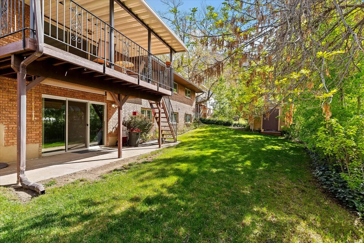 View of green lawn with a patio area, a balcony, and a shed