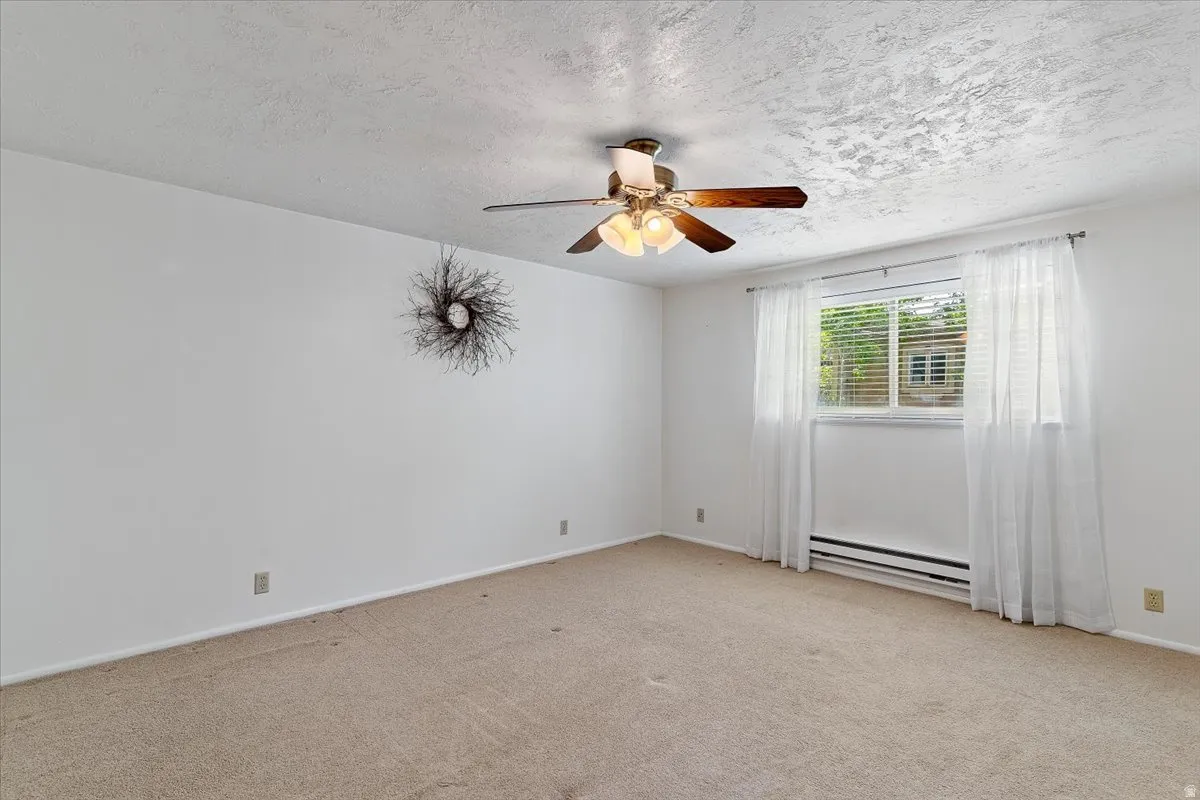 Carpeted empty room featuring ceiling fan, baseboard heating, and a textured ceiling