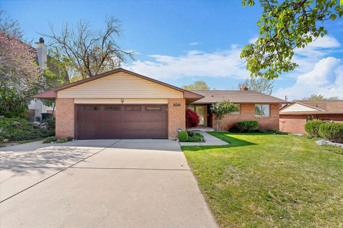 Single story home featuring a front yard, driveway, an attached garage, and brick siding