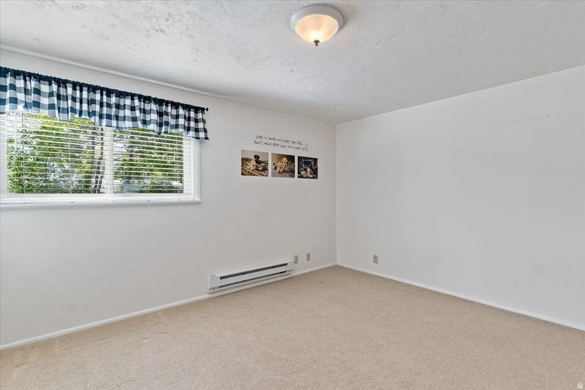 Empty room featuring a baseboard radiator, carpet floors, and a textured ceiling