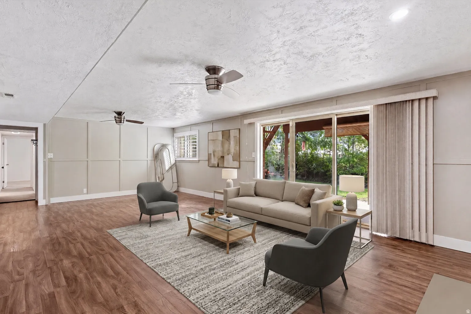 Spacious living area featuring wood-finish flooring, a full wall of sliding glass doors, and two ceiling fans