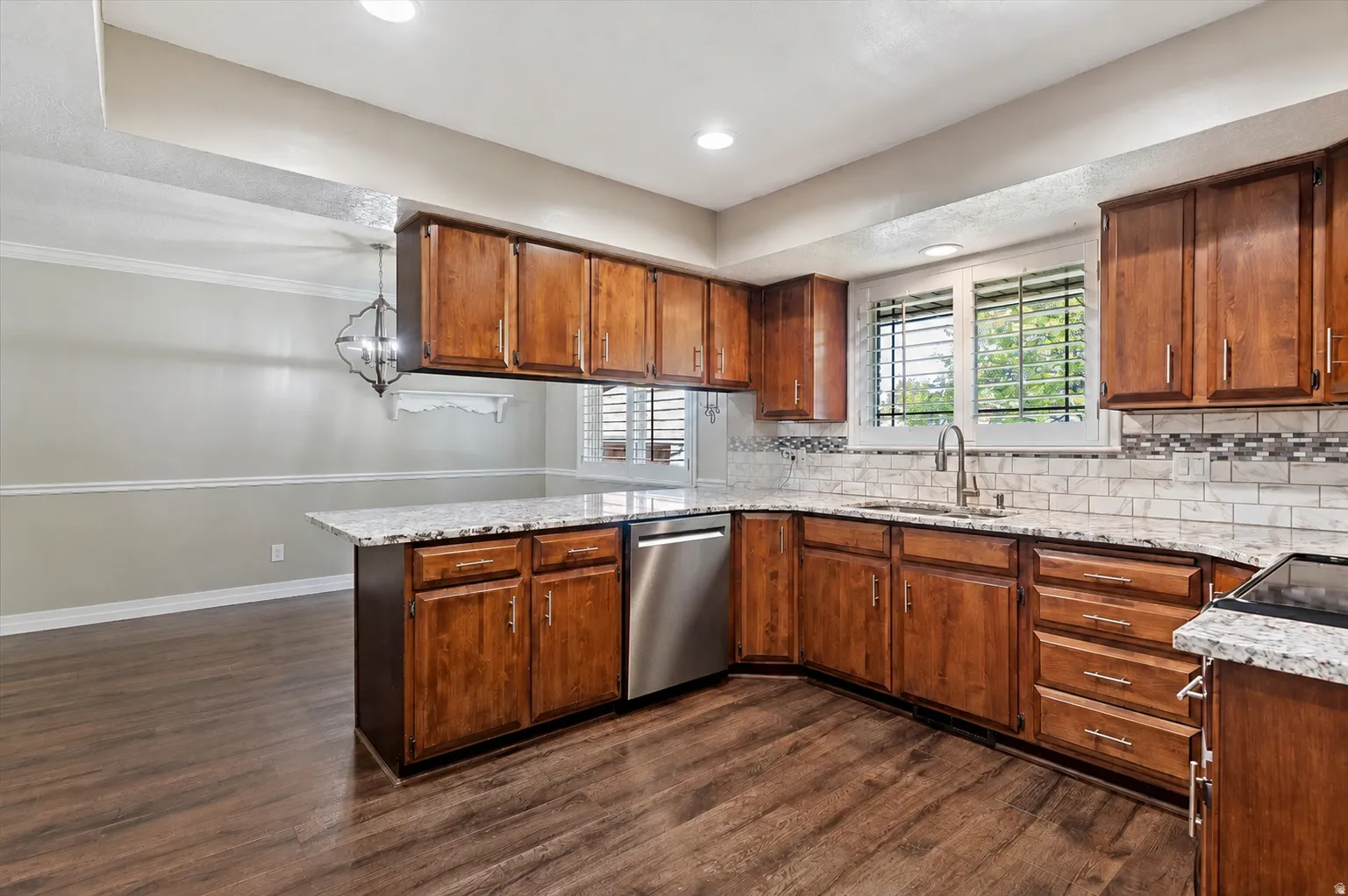 Kitchen featuring wood-finish flooring, ample wood cabinetry, light-toned countertops, subway tile backsplash, and stainless steel appliances