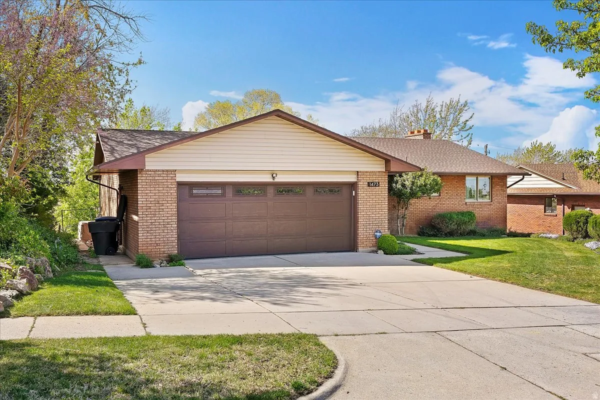 View of front of house featuring brick siding, concrete driveway, a chimney, a front lawn, and a garage