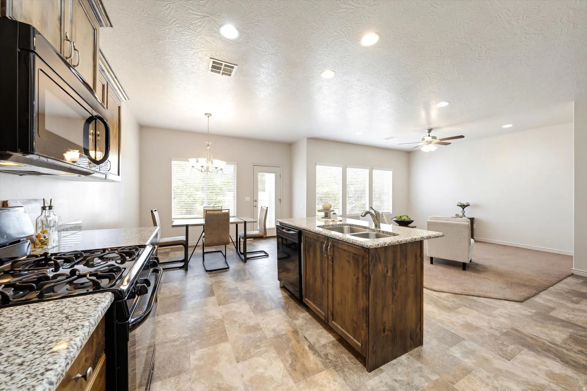 Kitchen featuring black appliances, a center island with sink, light stone countertops, a chandelier, and plenty of natural light