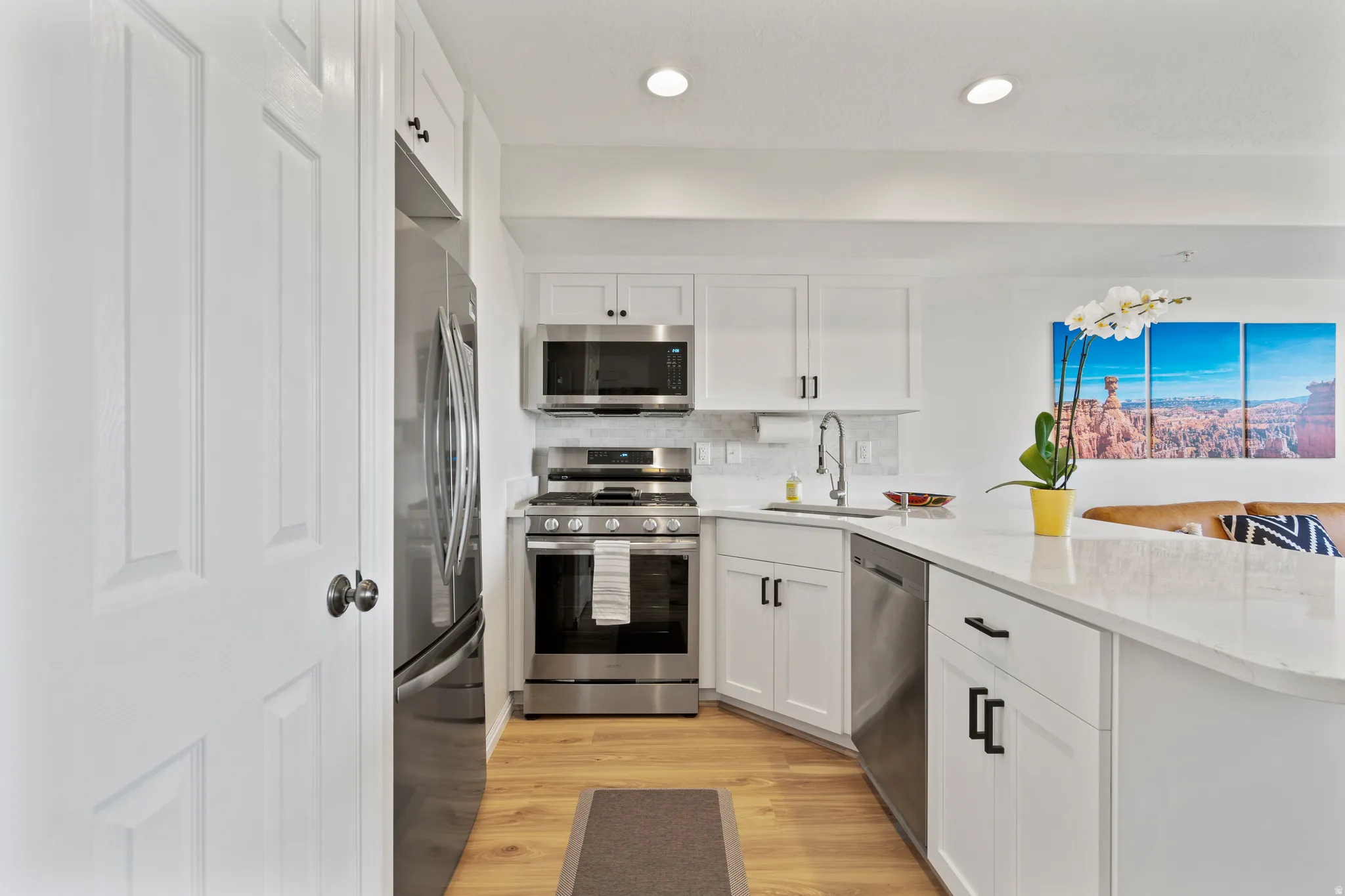 Kitchen with stainless steel appliances, white cabinets, a peninsula, and light wood finished floors