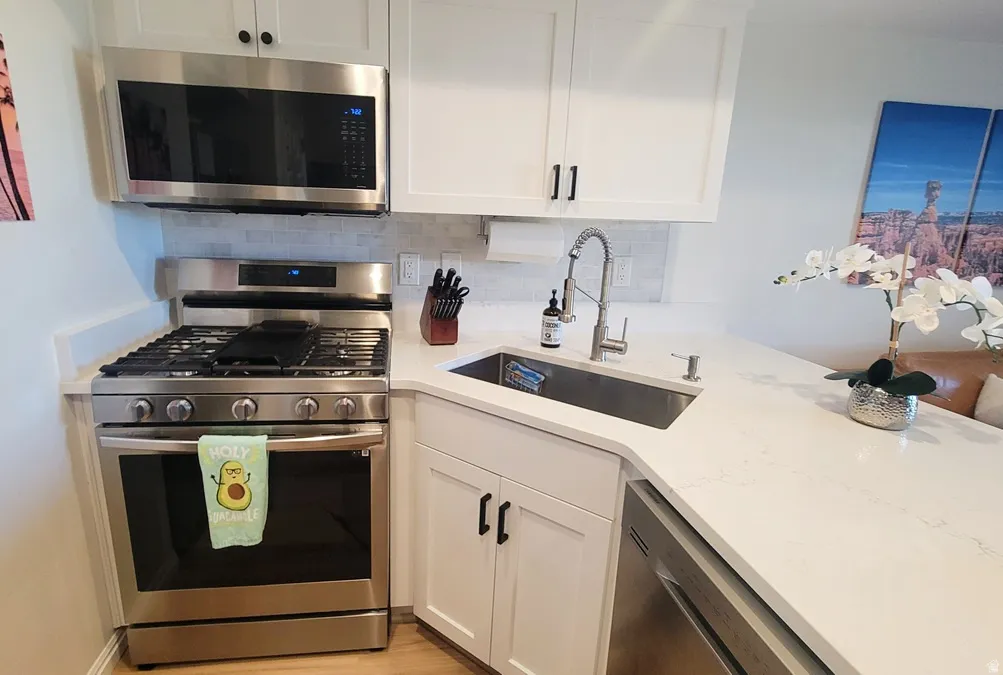 Kitchen with stainless steel appliances, white cabinetry, light stone counters, and tasteful backsplash