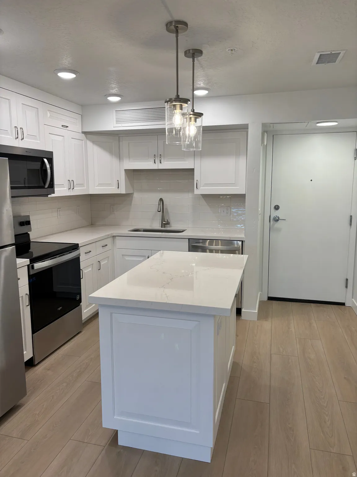 Kitchen featuring stainless steel appliances, light wood-style floors, decorative backsplash, pendant lighting, and white cabinetry
