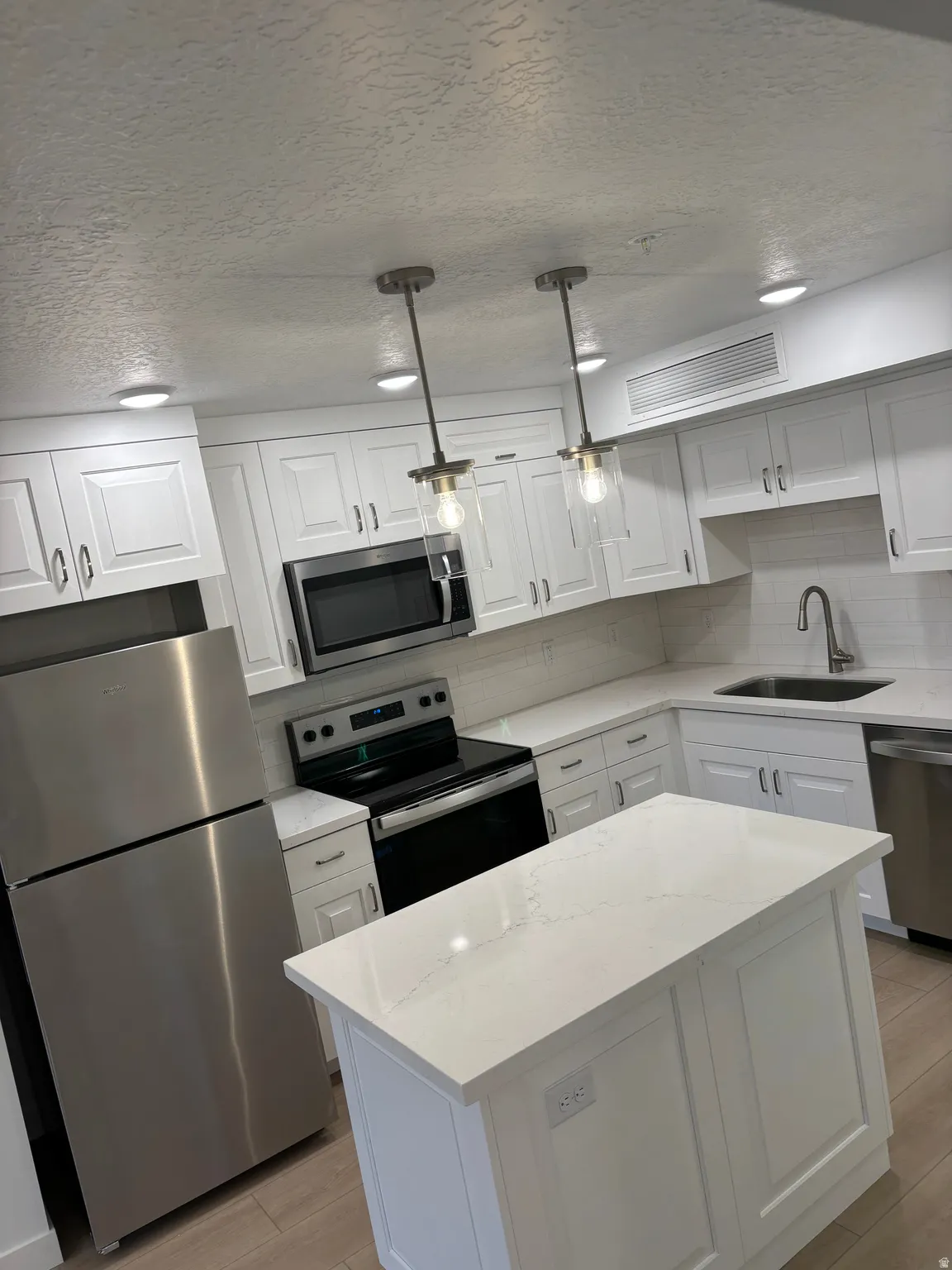 Kitchen featuring stainless steel appliances, white cabinetry, a textured ceiling, pendant lighting, and decorative backsplash
