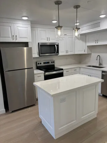 Kitchen featuring stainless steel appliances, white cabinets, hanging light fixtures, light wood-type flooring, and a center island