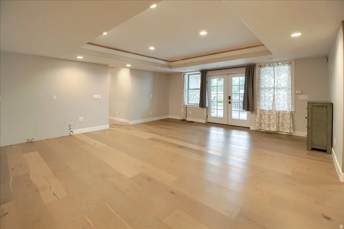 Empty room featuring french doors, light wood finished floors, recessed lighting, and a raised ceiling
