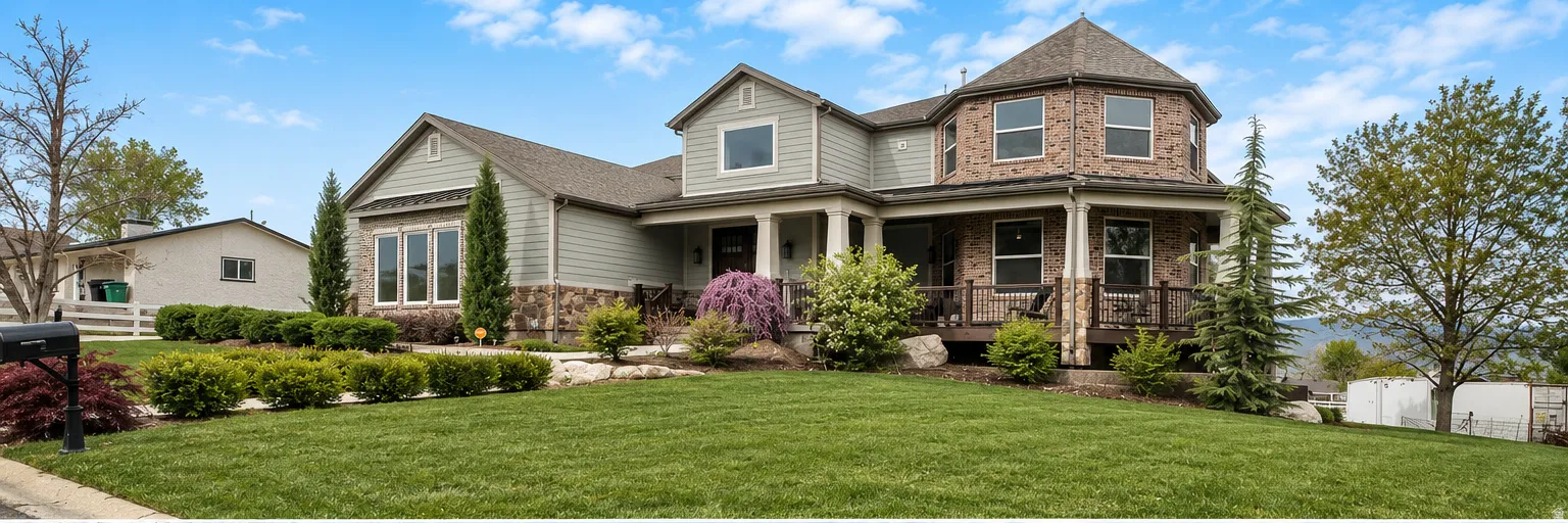 Spacious home featuring a multi-level design with a prominent octagonal turret, a combination of brick and siding exteriors, a covered porch with white columns, a manicured front lawn, and mature landscaping