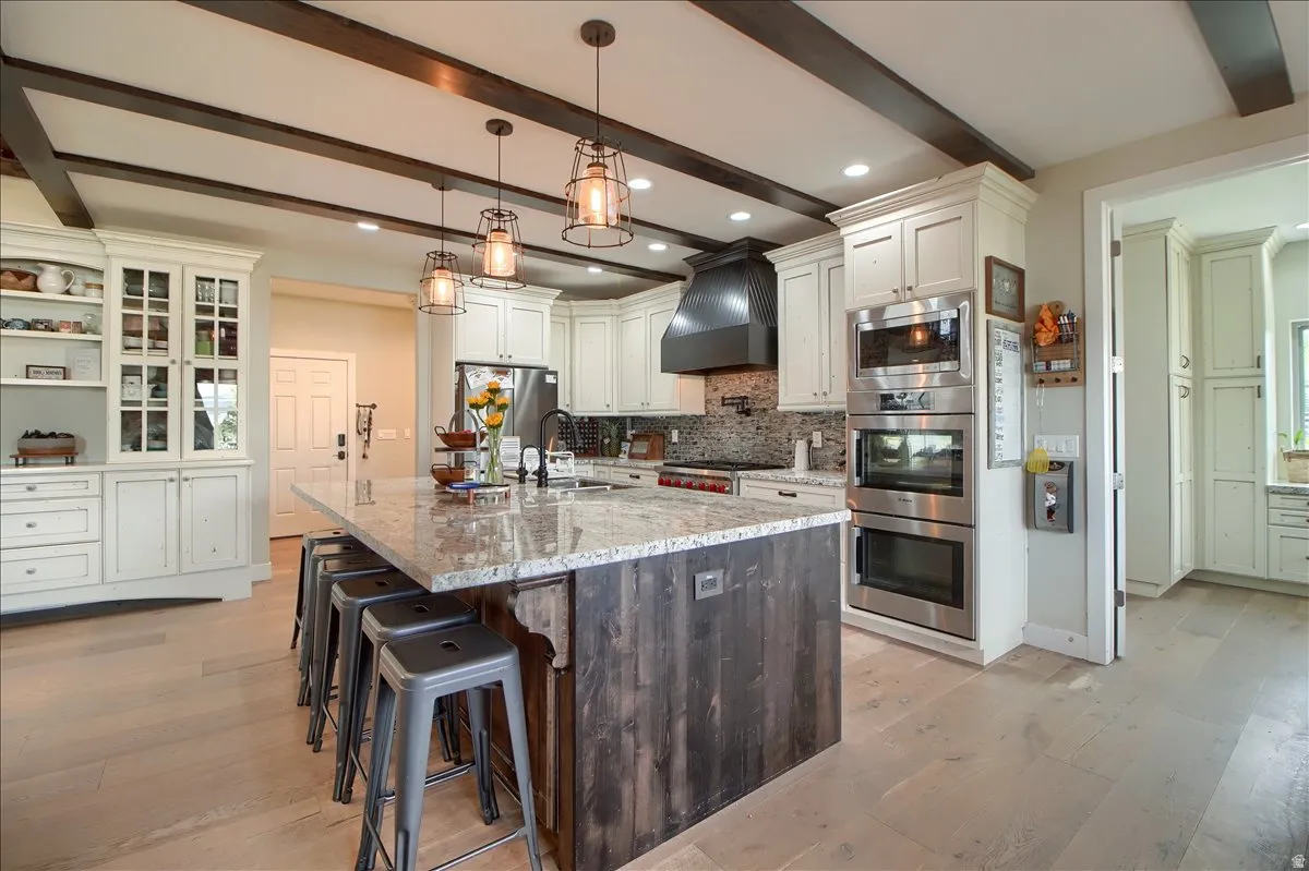 Kitchen featuring dual tone cabinets, a kitchen bar, light stone countertops, a kitchen island with sink, and light wood finished floors