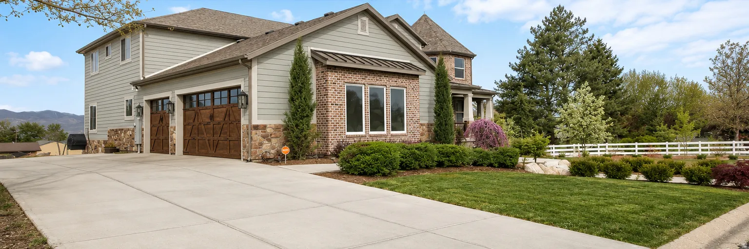 Crafted exterior featuring a combination of brick and siding, a multi-car driveway, decorative garage doors, and mature landscaping