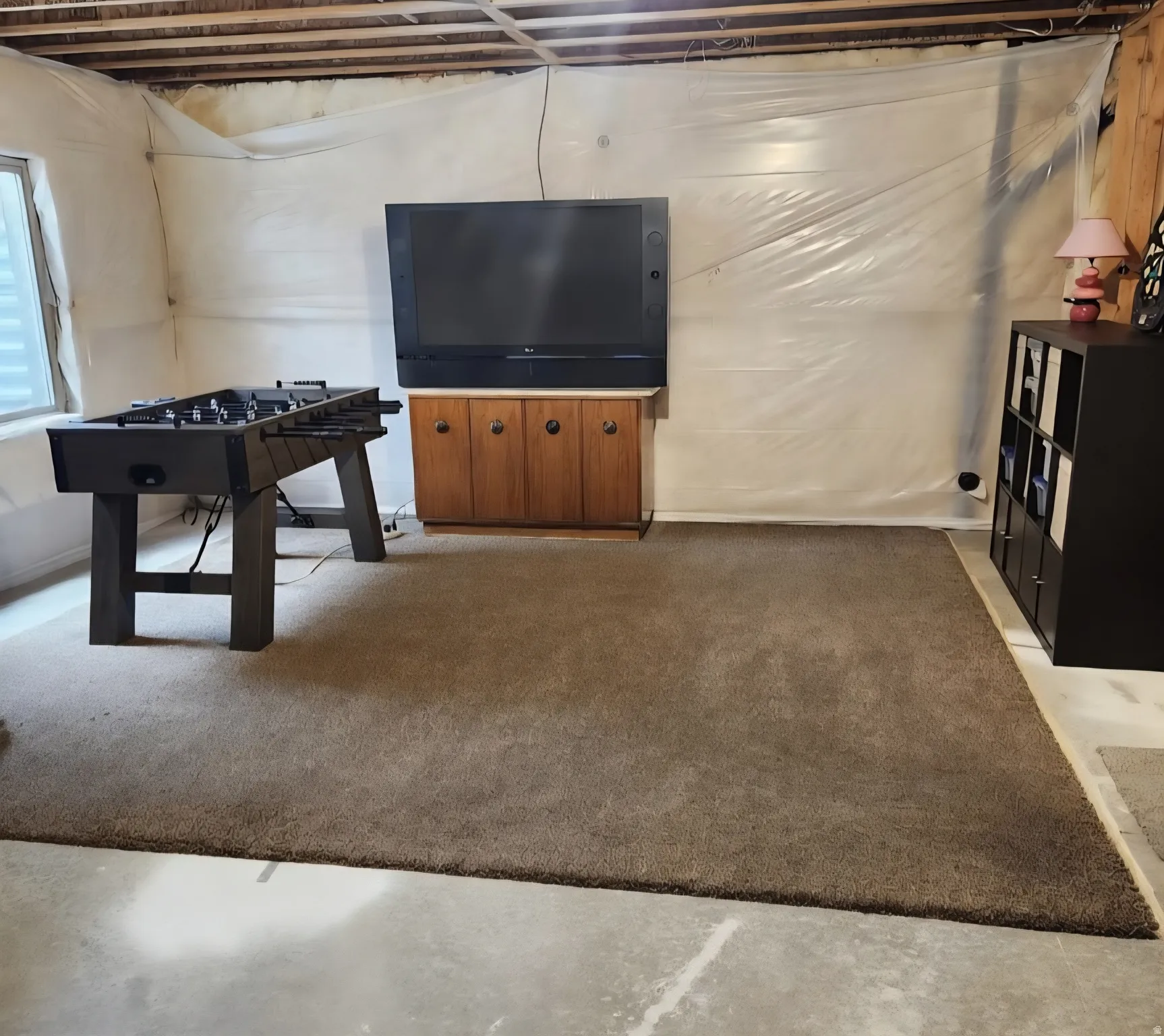 Carpeted area with a window, wooden ceiling joists, and a partial wood-paneled wall