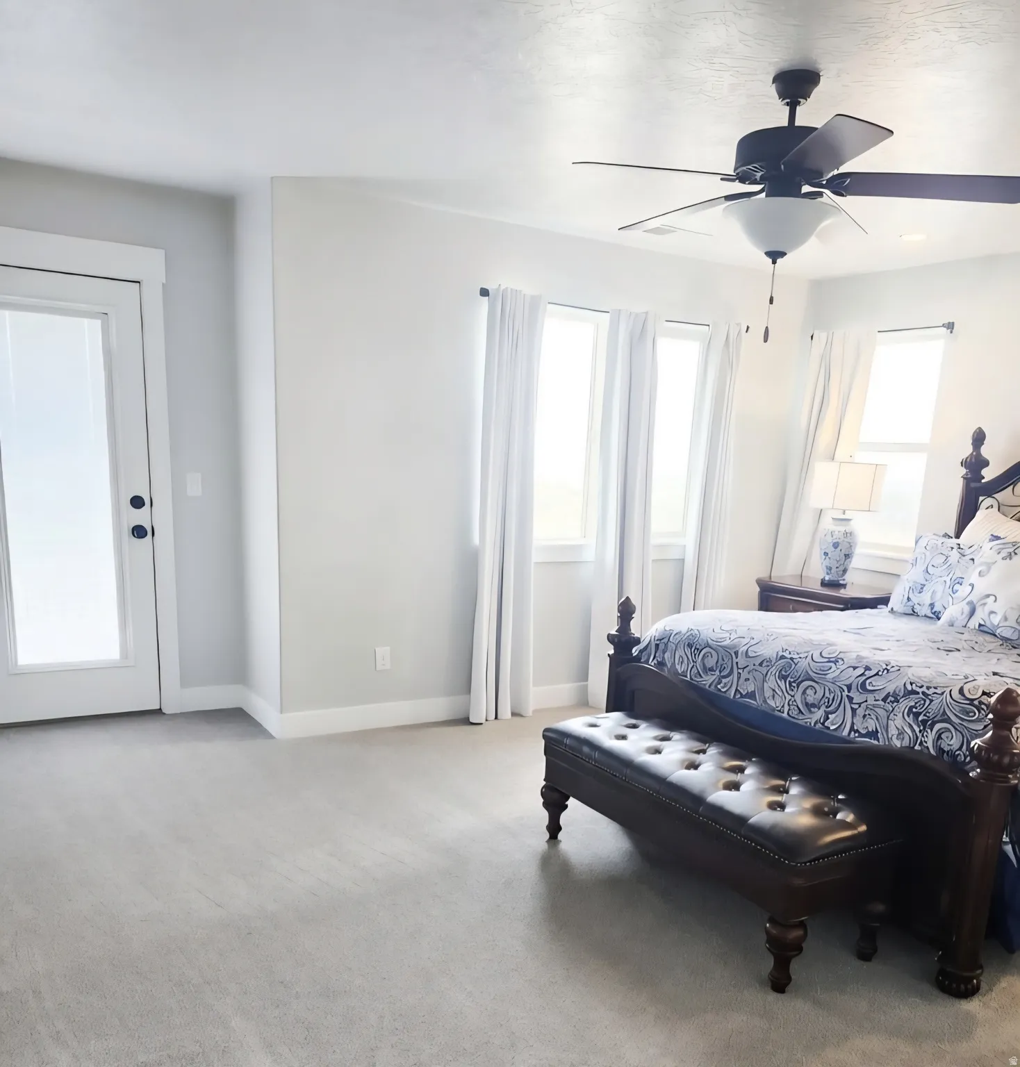 Bedroom featuring light-toned carpeting, a ceiling fan with integrated lighting, multiple windows with white trim, a white egress door with frosted glass, and white baseboards