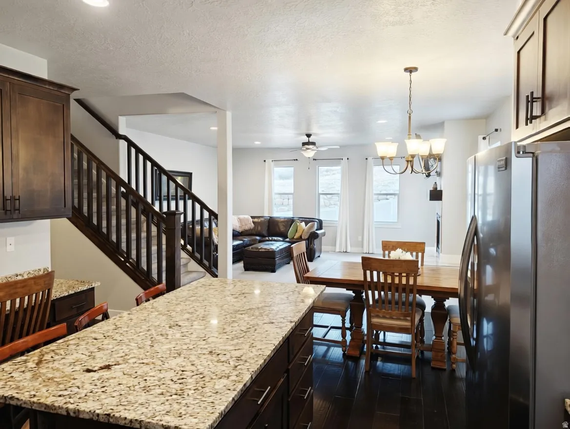Kitchen island with granite countertop, dark wood-finish cabinetry, and stainless steel refrigerator