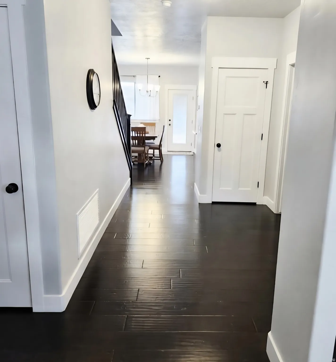 Hallway featuring dark wood-finish flooring, white baseboards, and white paneled doors with black hardware