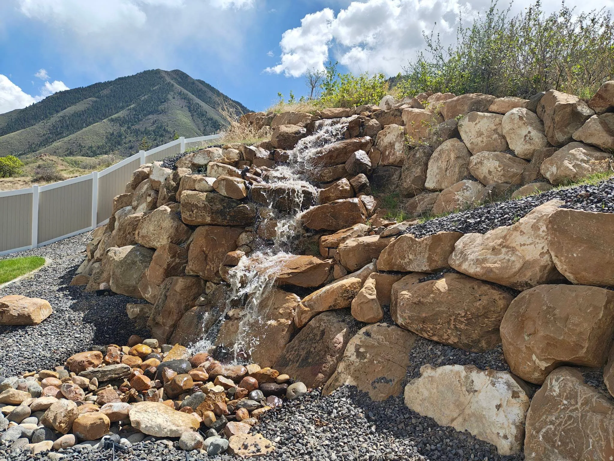 Natural rock waterfall feature surrounded by decorative gravel and a variety of river stones