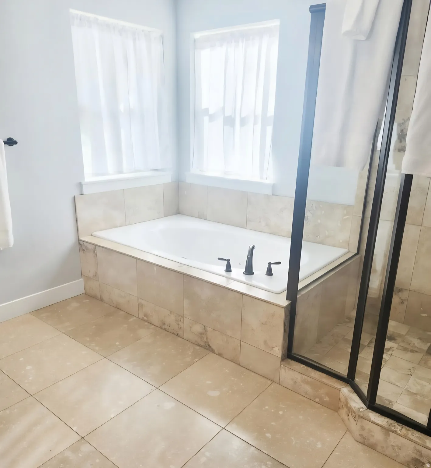 Soaking tub with tile surround, framed by two large windows and matte black fixtures